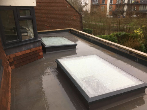 Two flat roof skylights on a rooftop with surrounding buildings in the background.